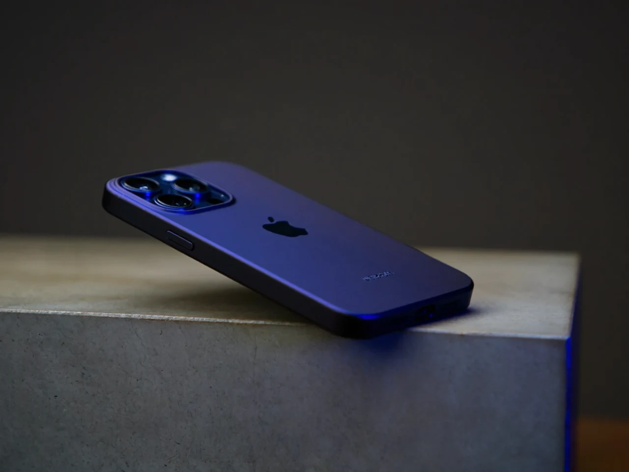 Smartfon w ciemnym etui spoczywa ukośnie na betonowej płycie w chłodnym świetle bocznym.